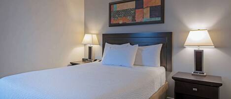 A neatly made bed with white linens, two bedside tables with lamps, and a colorful abstract painting on the wall.