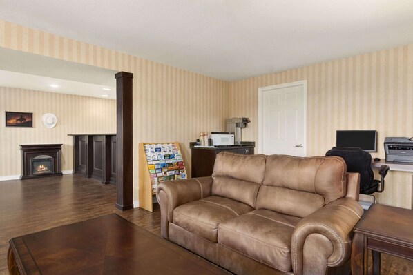 A living room with a leather sofa, a fireplace, a wall-mounted TV, and a door. - Travelodge by Wyndham Kamloops Mountview (Kamloops)