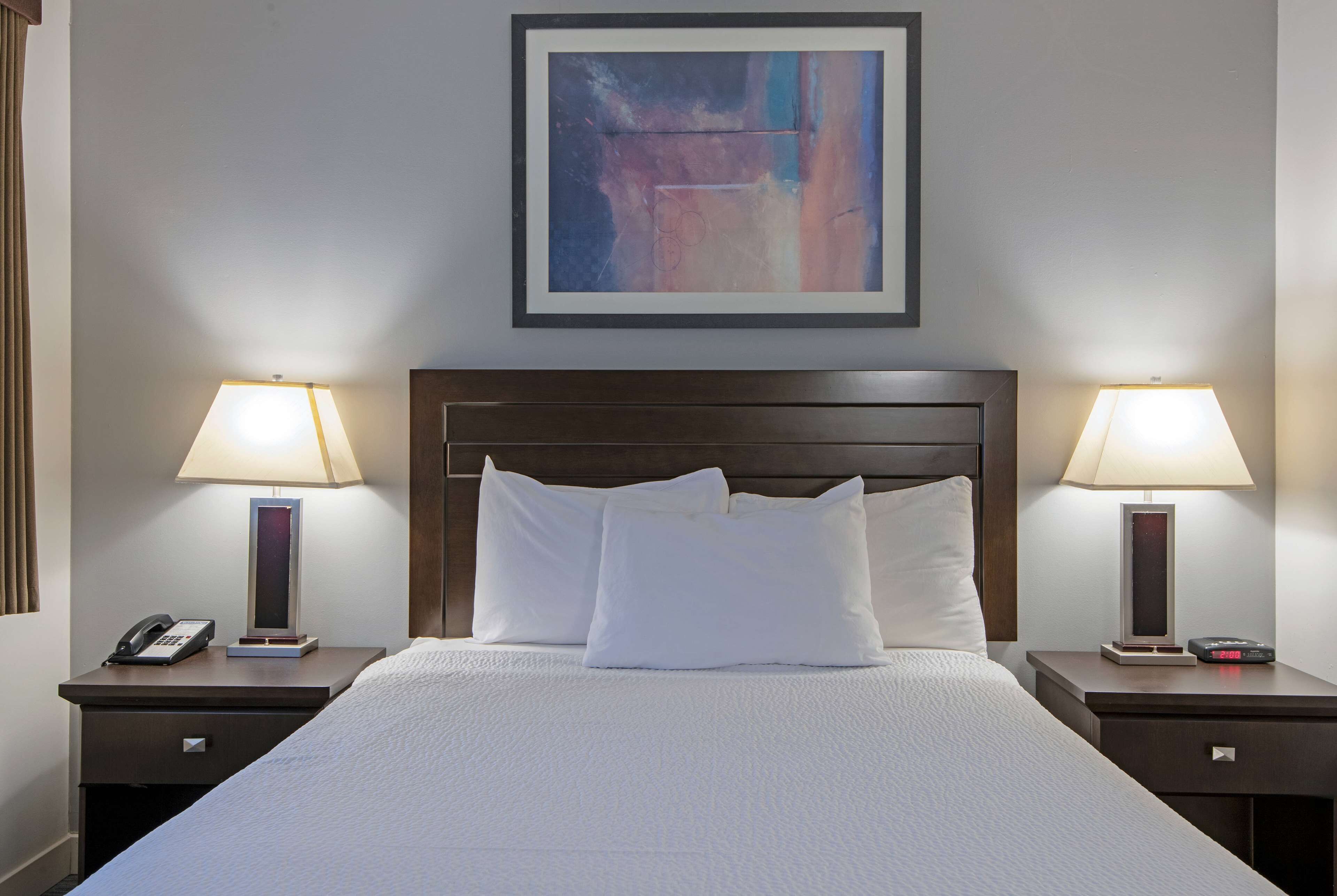Camera d'albergo con un letto grande, due comodini con lampade, un telefono e un quadro astratto incorniciato appeso al muro.