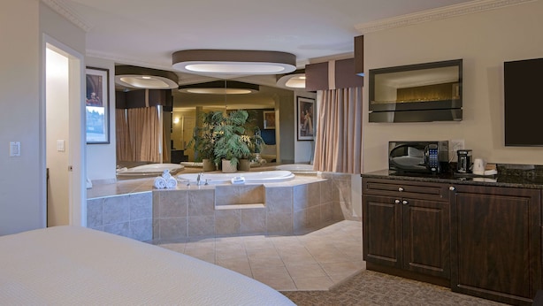 A modern hotel room with a large bed, a sitting area with a view of a jacuzzi, a kitchenette, and a large mirror.