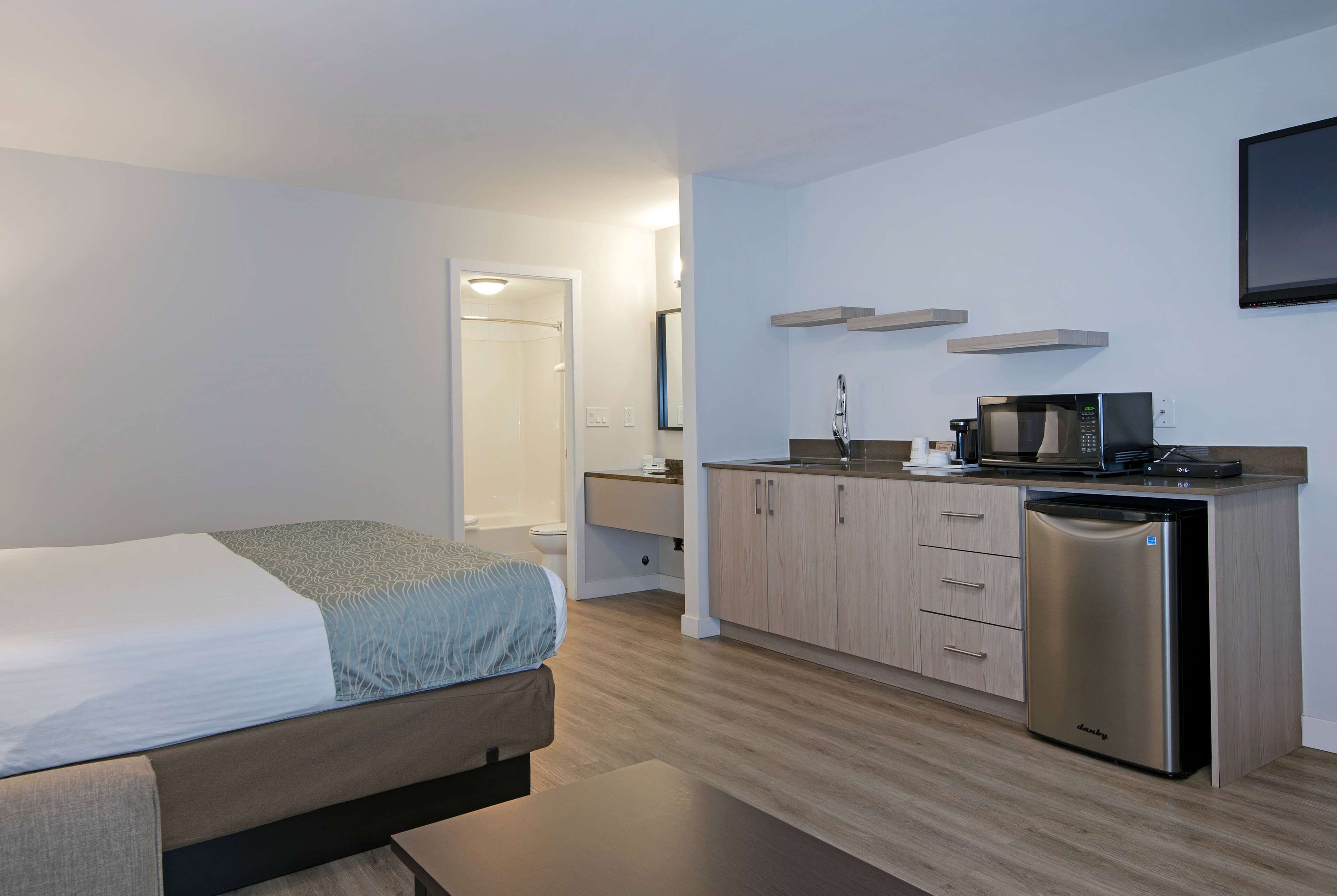 A compact hotel room with a bed, a small kitchenette, and a bathroom.