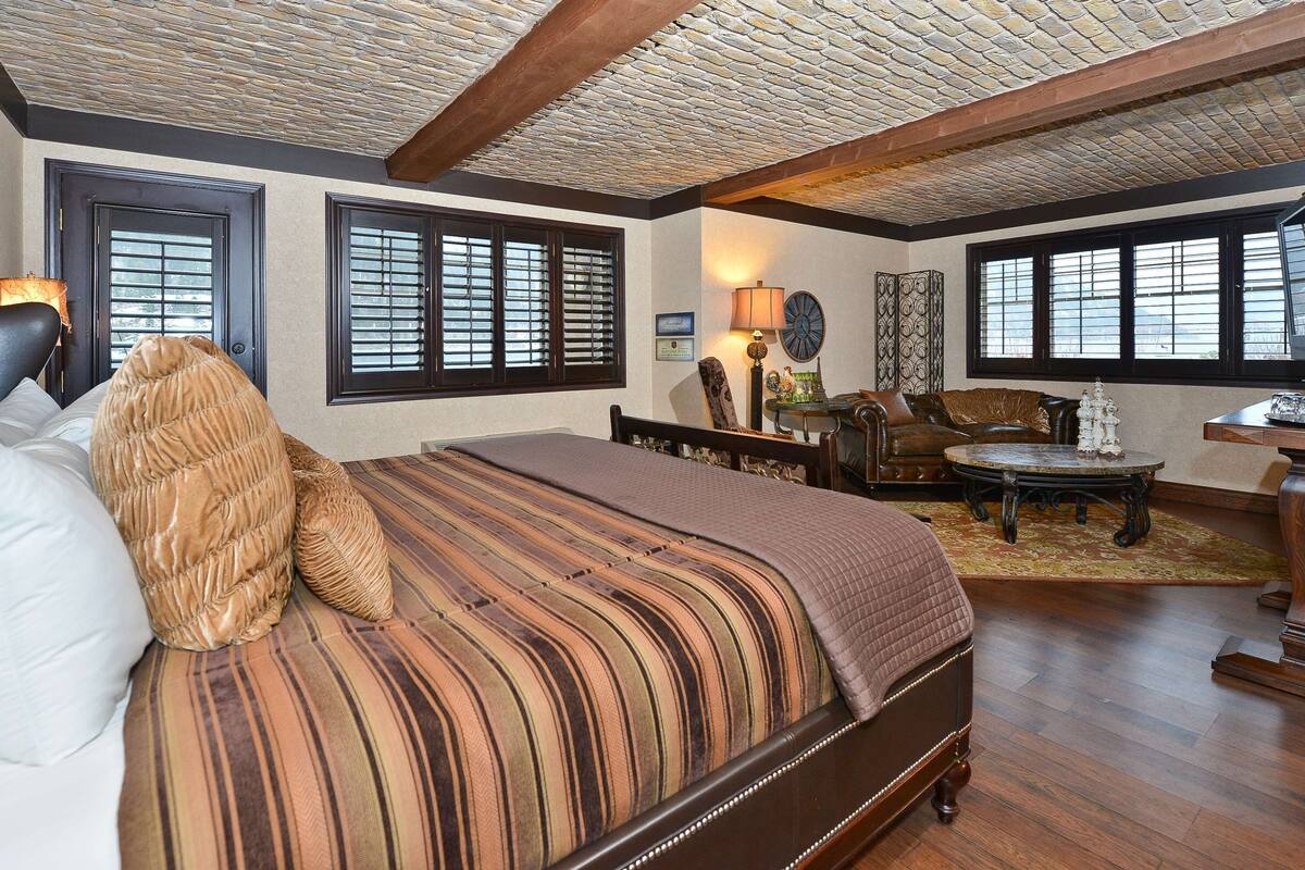 Quarto com uma cama grande, uma mesa de centro de madeira, um sofá de couro e uma televisão.