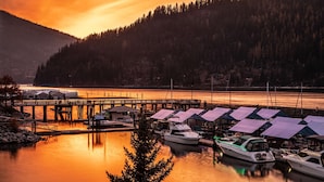 Una marina con barcos amarrados, un muelle de madera y un promontorio boscoso al fondo.