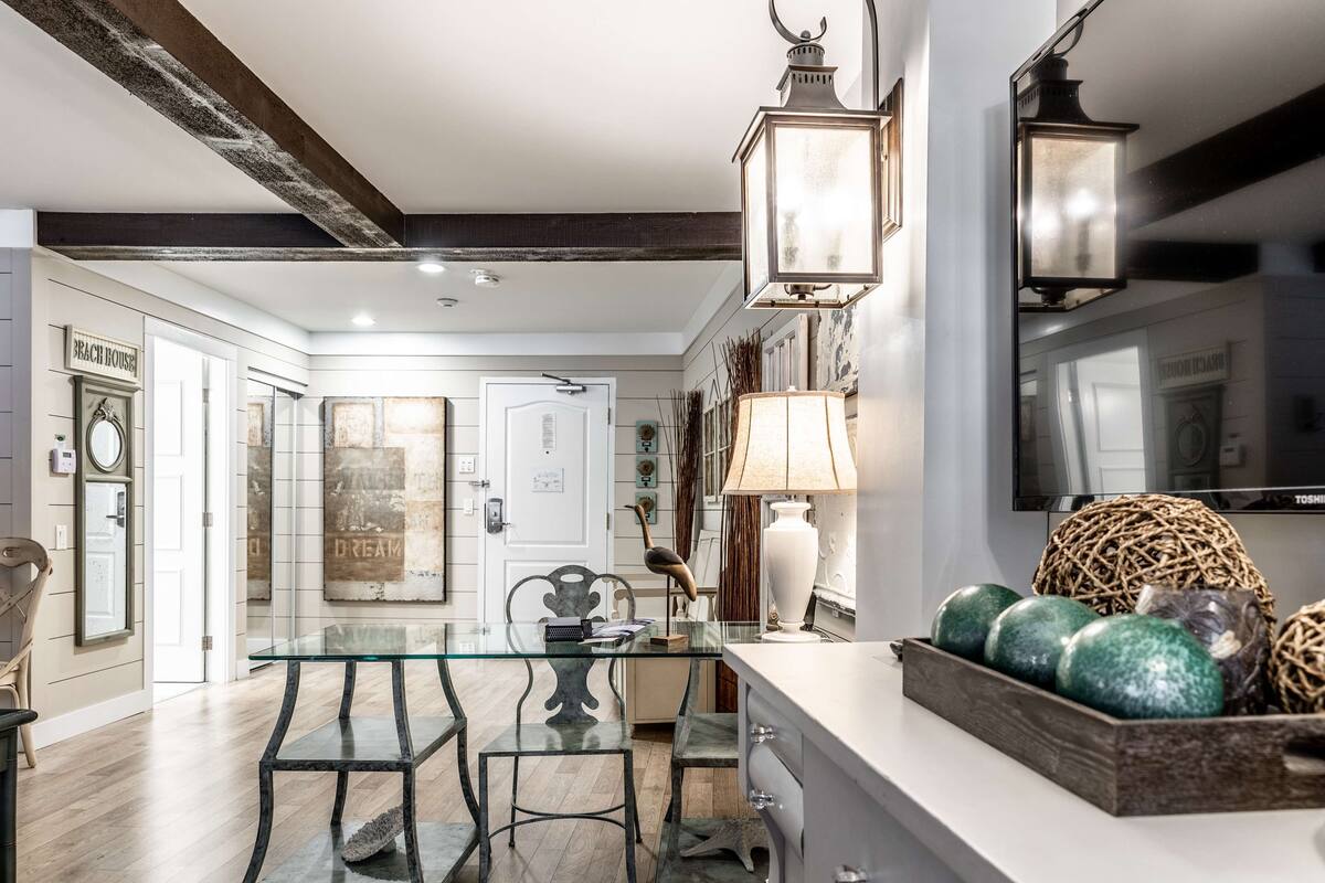 Cozinha moderna com mesa de vidro, duas cadeiras, bancada branca e objetos decorativos.