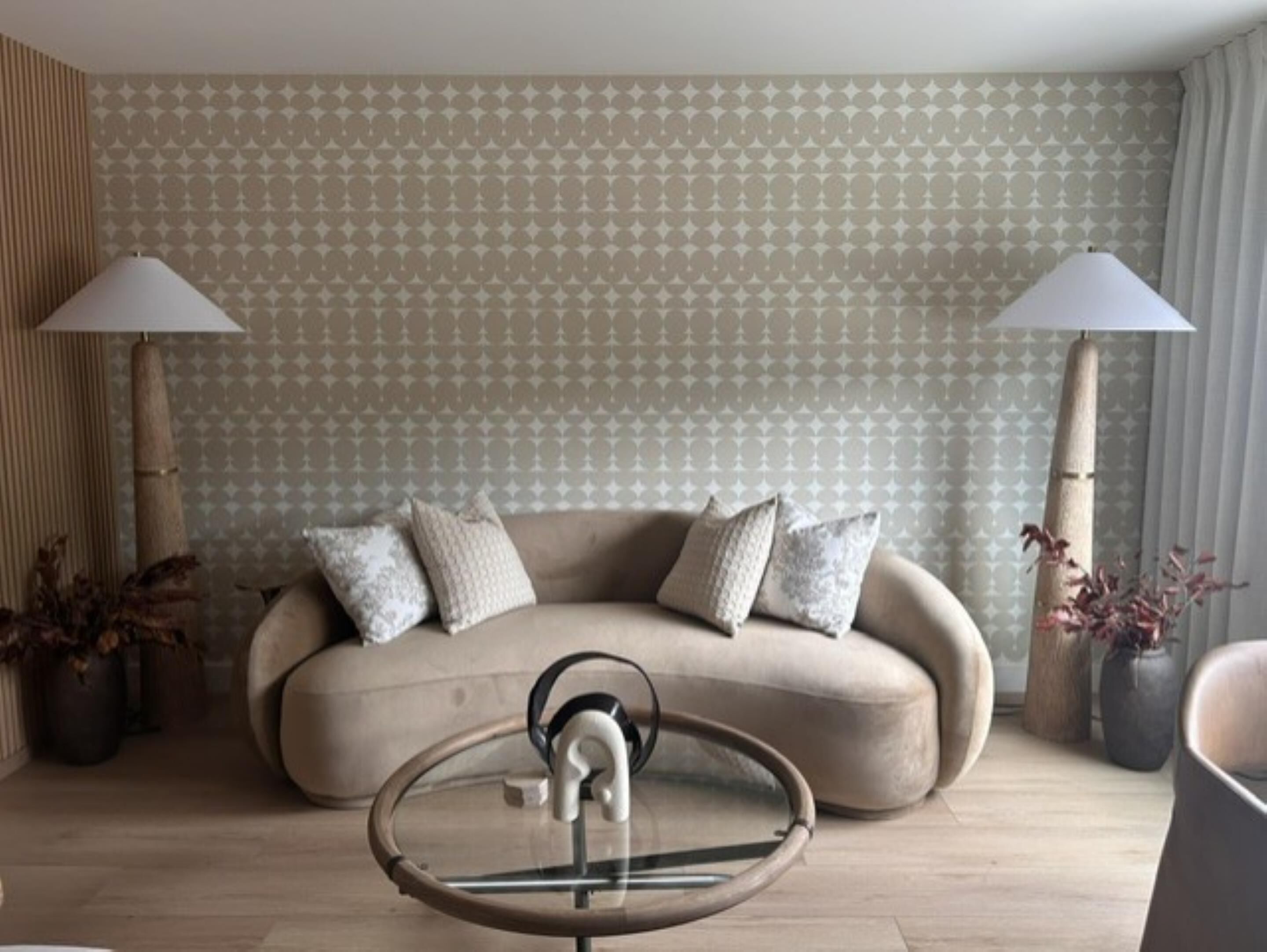 A living room with a sofa, two lamps, a glass coffee table, and patterned wallpaper.