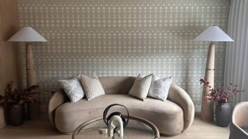 A living room with a sofa, two lamps, a glass coffee table, and patterned wallpaper.