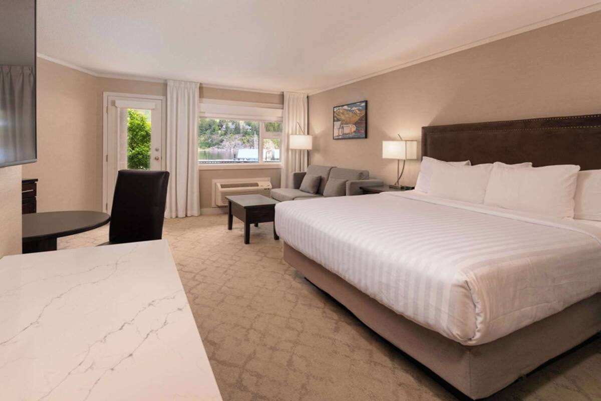 Quarto de hotel com uma cama grande, uma escrivaninha, uma cadeira, um sofá e uma televisão.