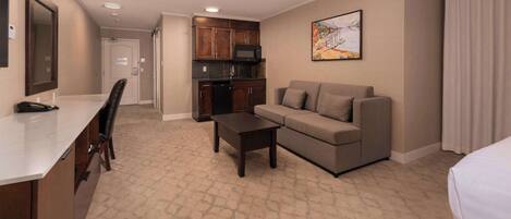 A hotel room with a kitchenette, a sofa, a coffee table, and a bed.