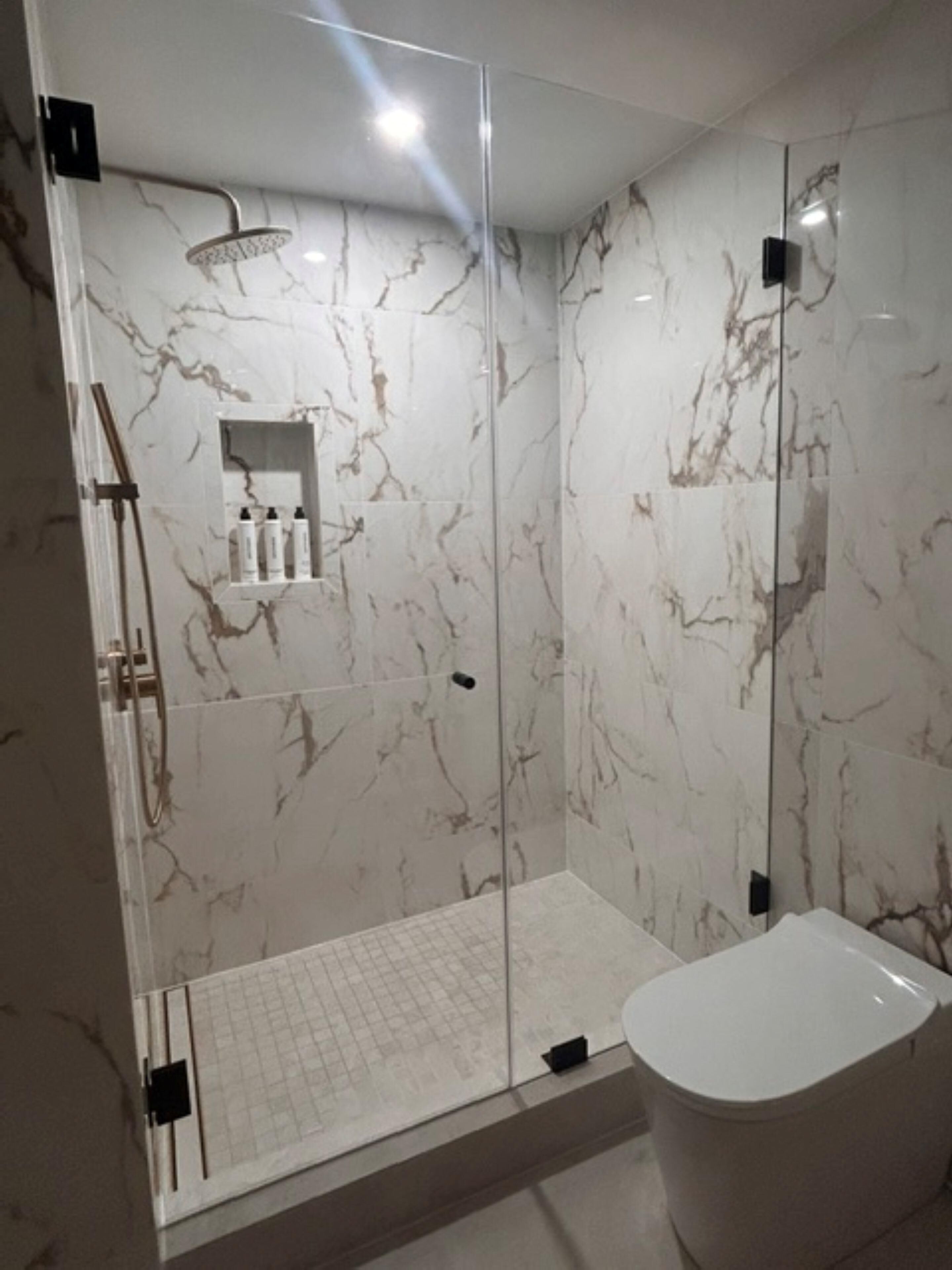A modern bathroom with a glass-enclosed shower, a marble-tiled wall, and a white bathtub.