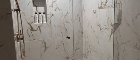 A modern bathroom with a glass-enclosed shower, a marble-tiled wall, and a white bathtub.