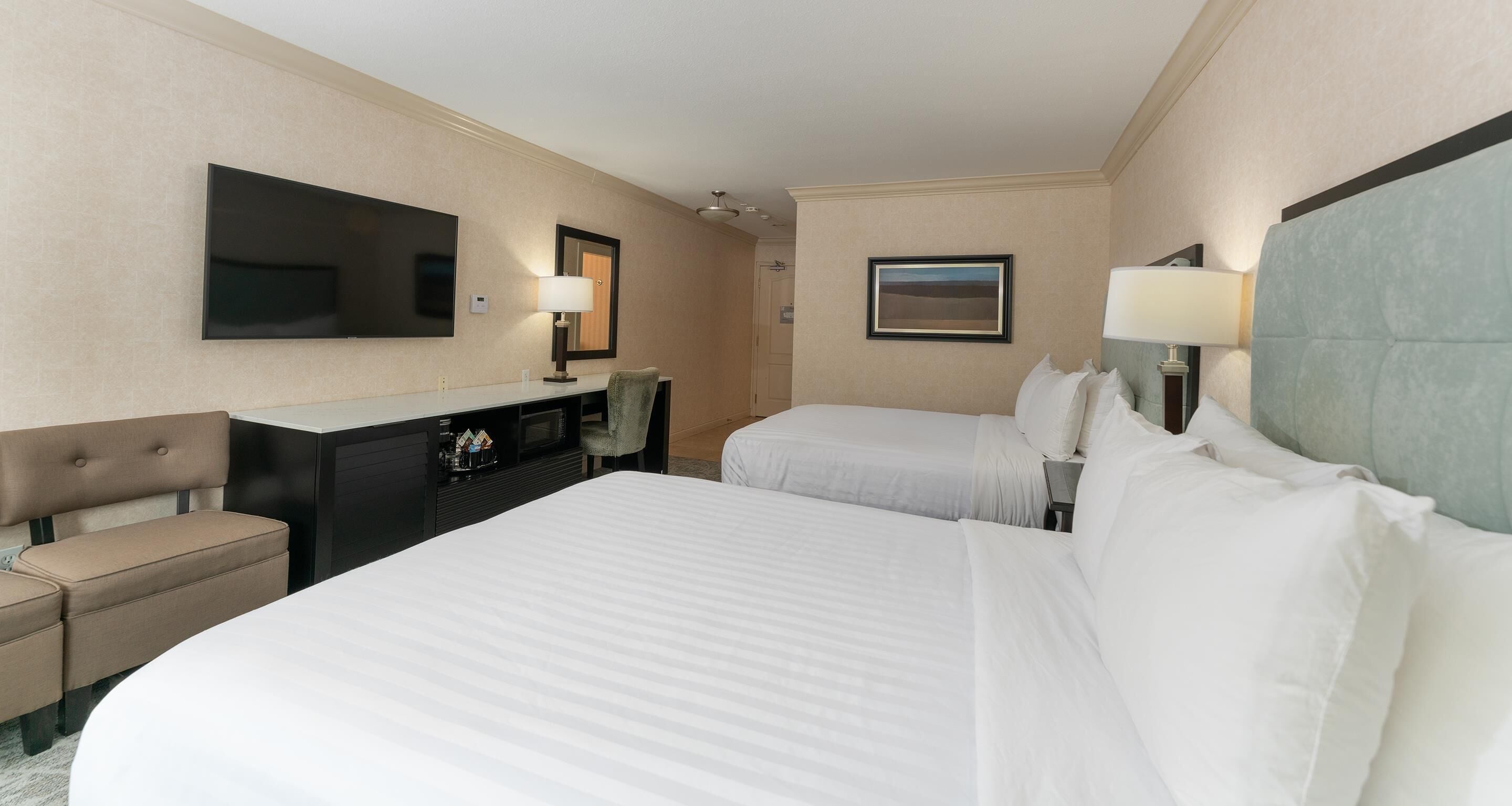 Ein Hotelzimmer mit zwei Betten, einem Schreibtisch, einem Stuhl, einem Fernseher und zwei Lampen.