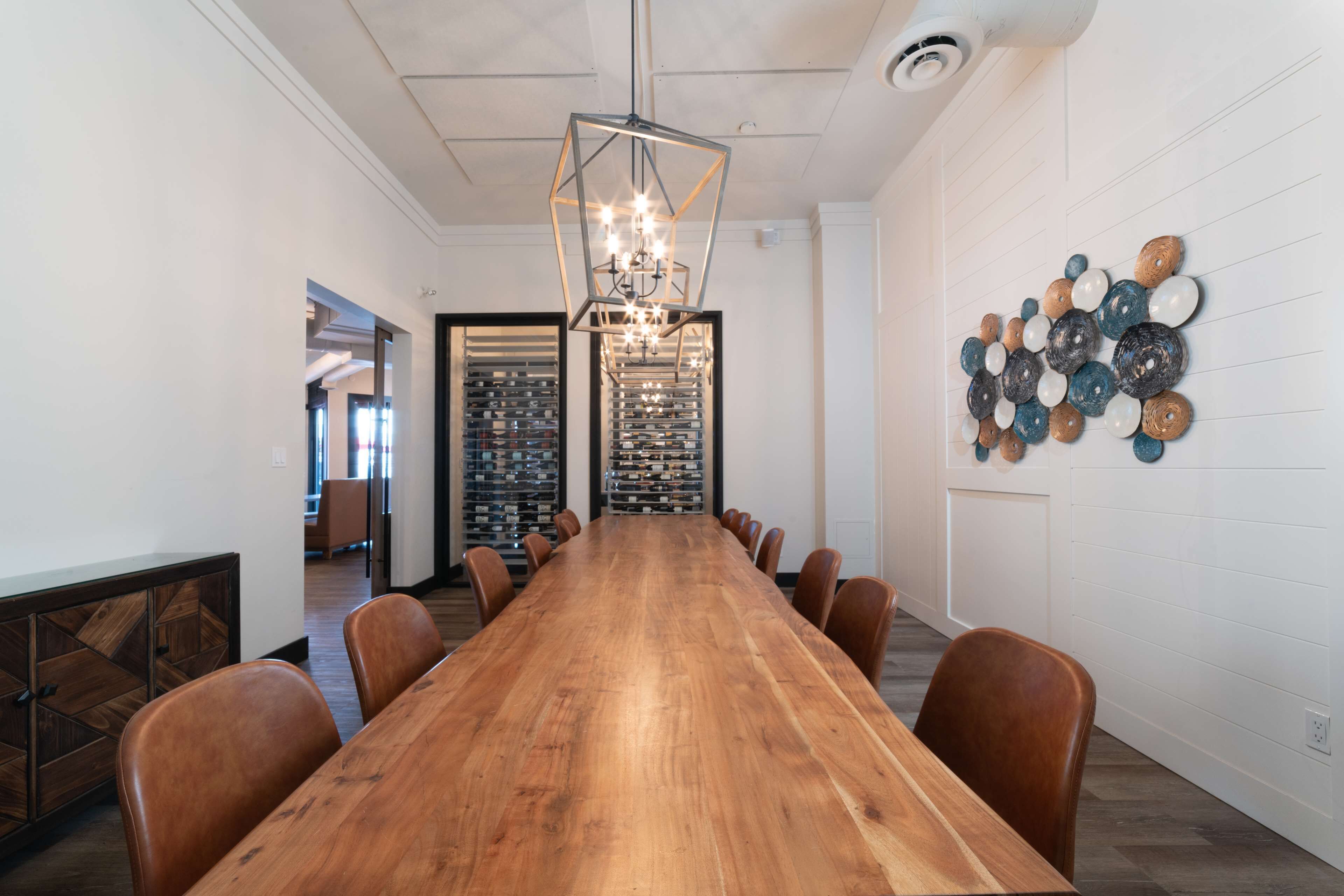 A long wooden conference table with chairs, a geometric chandelier, and a wall-mounted decorative arrangement.