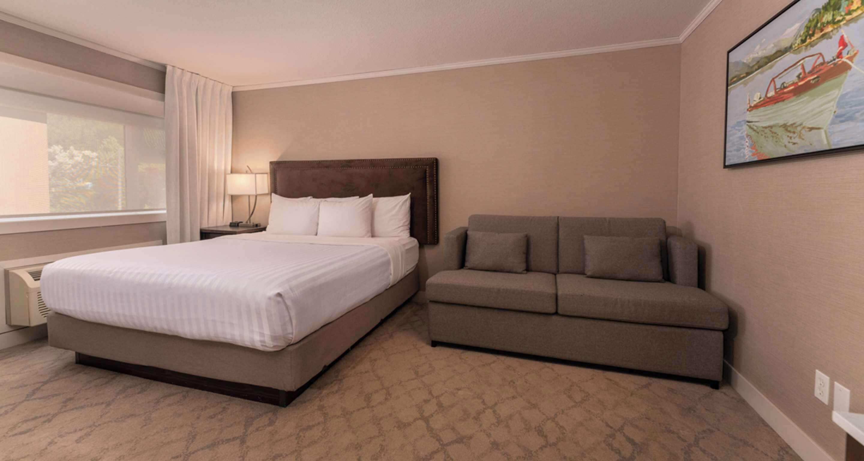 Une chambre d’hôtel avec un lit, un canapé, une table de chevet, une lampe et un tableau au mur.