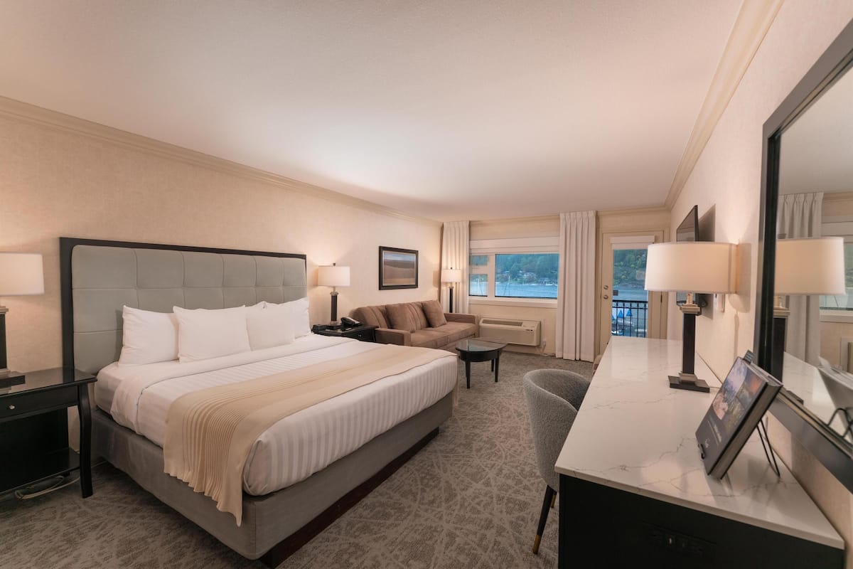 Quarto de hotel com uma cama grande, um sofá, uma escrivaninha e uma cadeira. Há uma janela com vista para o exterior.