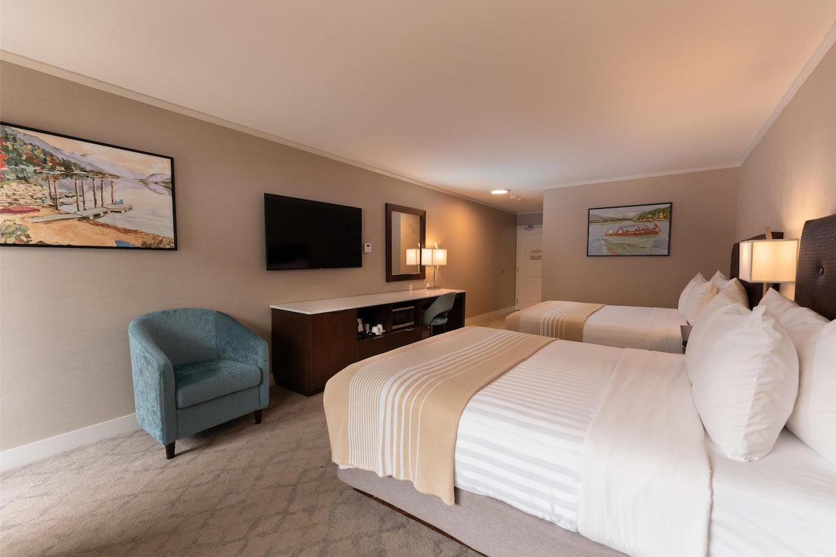 Quarto de hotel com duas camas, uma escrivaninha, uma cadeira e obras de arte nas paredes.