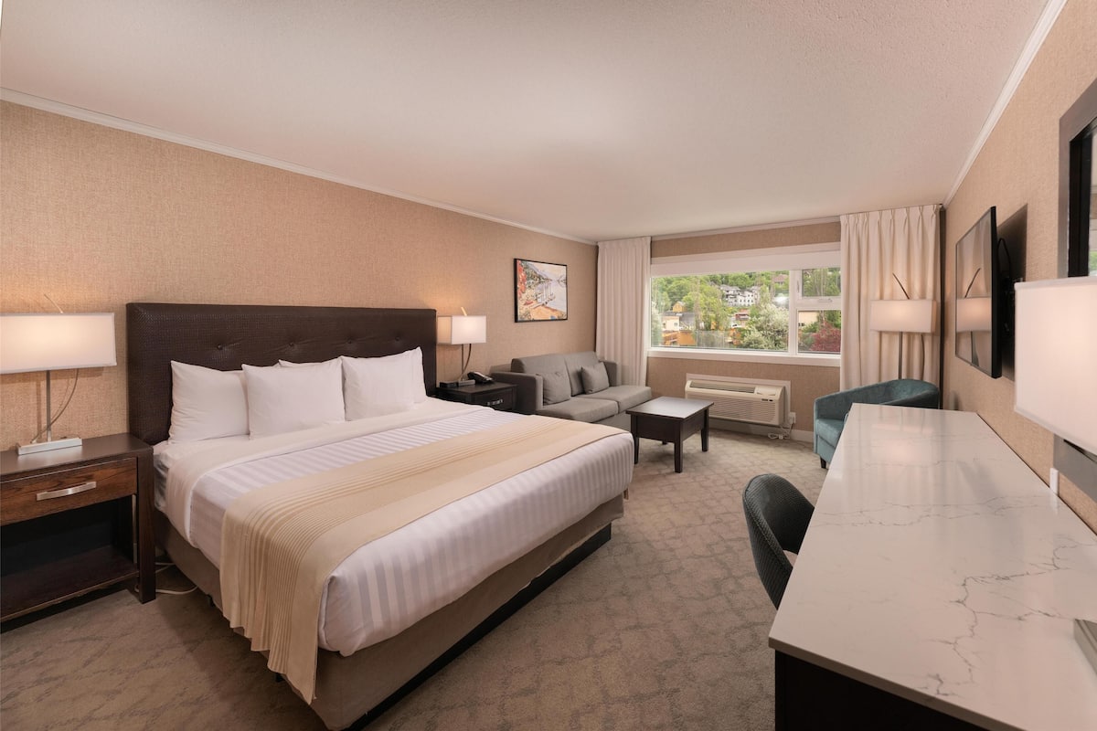 Quarto de hotel com uma cama grande, um sofá, uma escrivaninha e vista para o exterior.