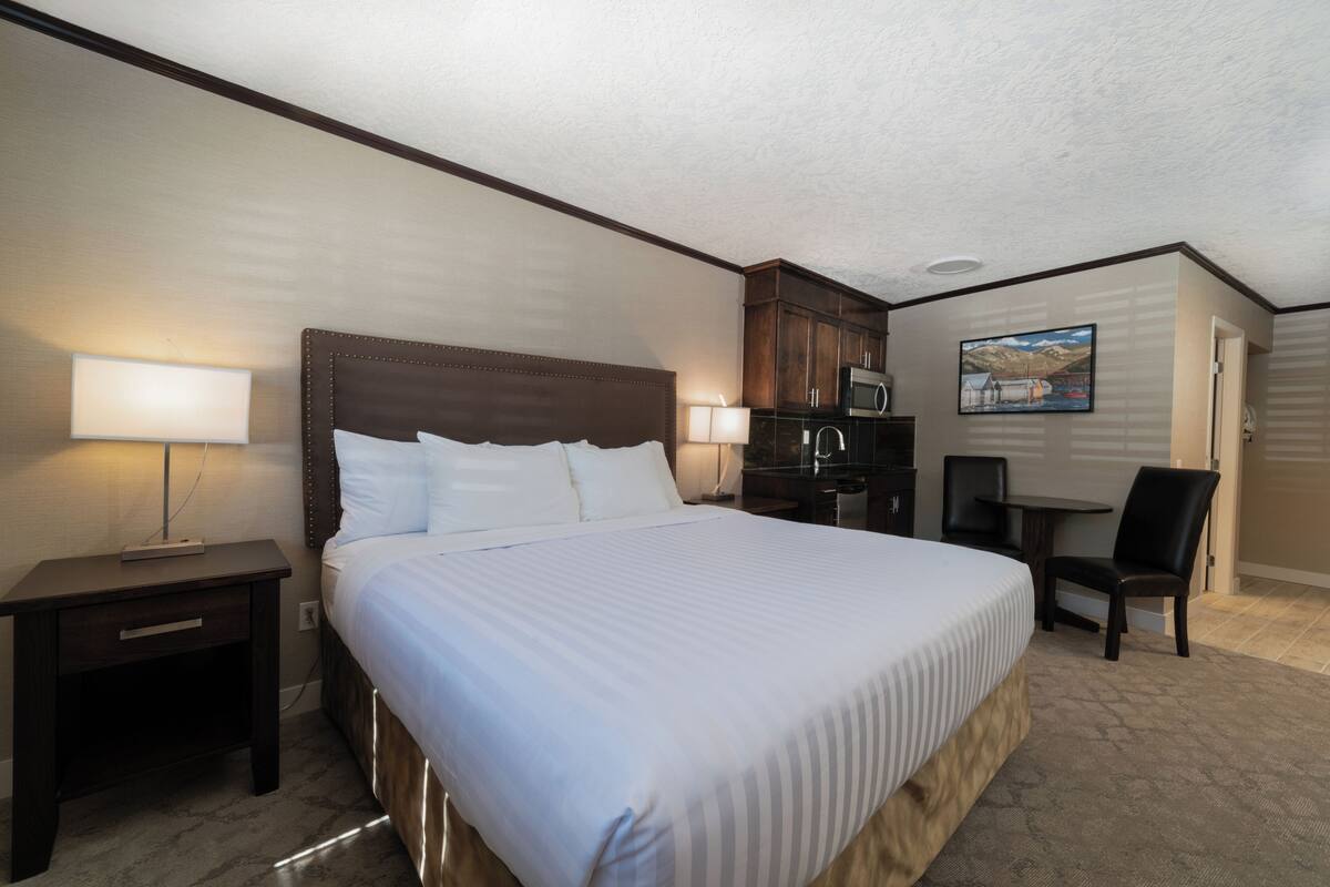 Quarto de hotel com uma cama grande, uma escrivaninha, uma cadeira, um micro-ondas e um quadro na parede.