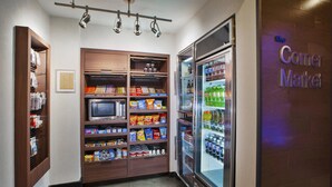 Eine Ecke einer Hotelhalle mit einer Minibar, einem mit Getränken gefüllten Kühlschrank und einem Schild für 'The Corner Market'.