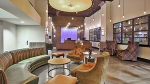 Eine großzügige Lobby mit einem gebogenen, grünen Sofa, mehreren Sesseln und einem Empfangstresen mit blauer Beleuchtung.