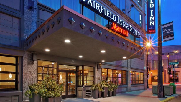 Das Hotel Fairfield Inn & Suites mit auffälligem Marquee-Schild, großen Fenstern und Topfpflanzen am Eingang.