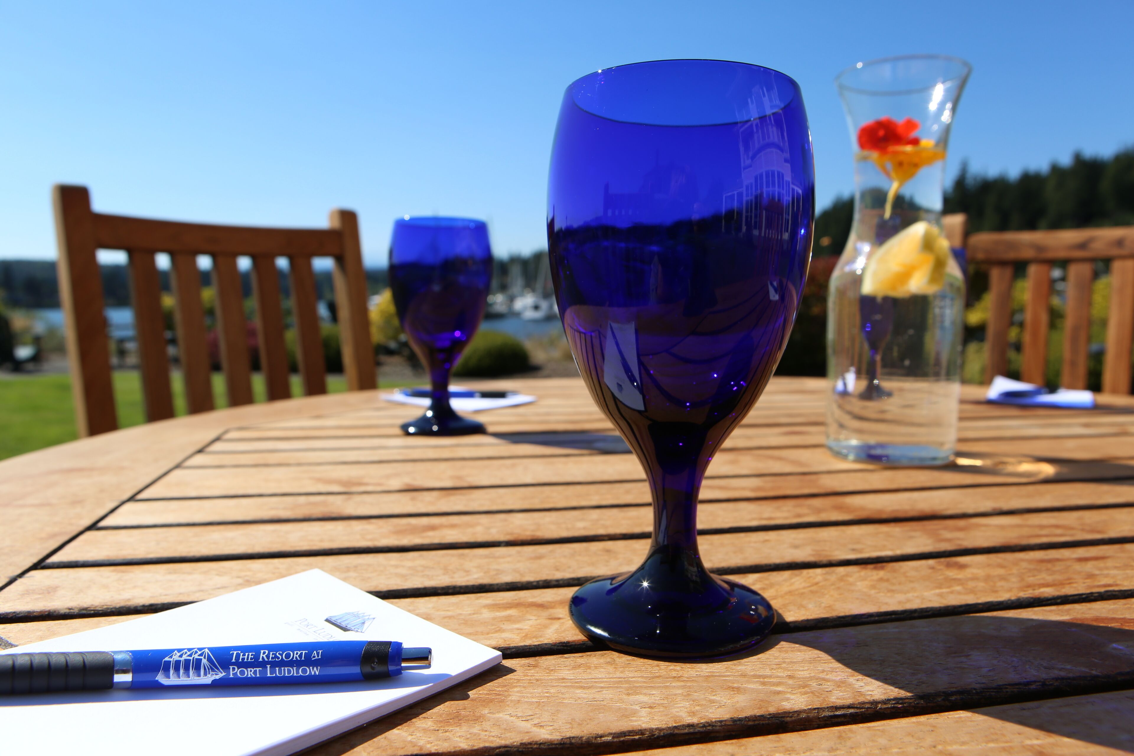 A wooden table with two blue glassware items and a pen on a notepad.