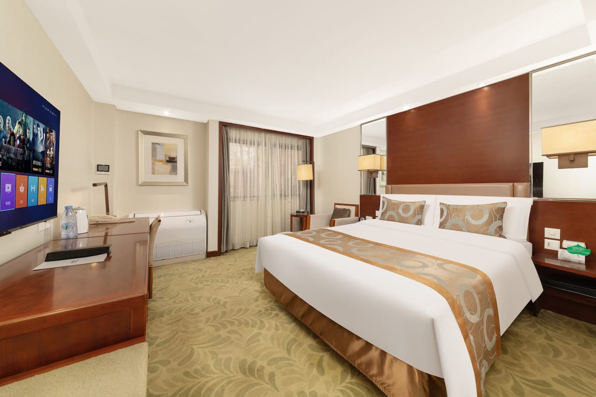 Ein Hotelzimmer mit einem großen Bett, einem Schreibtisch, einem Sessel, einem Fernseher und einem Fenster mit Vorhängen.