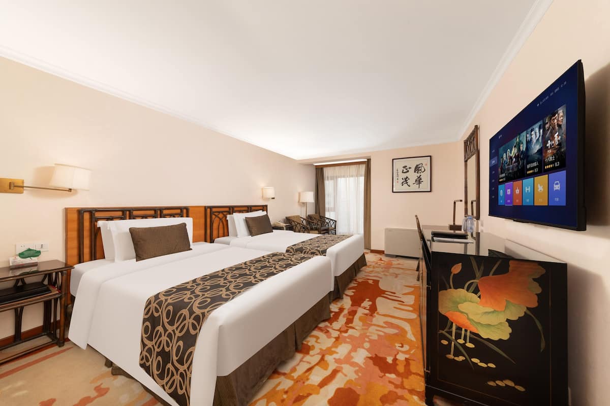 Ein Hotelzimmer mit zwei Betten, einem Fernseher, einem Schreibtisch und einem dekorativen Schrank.