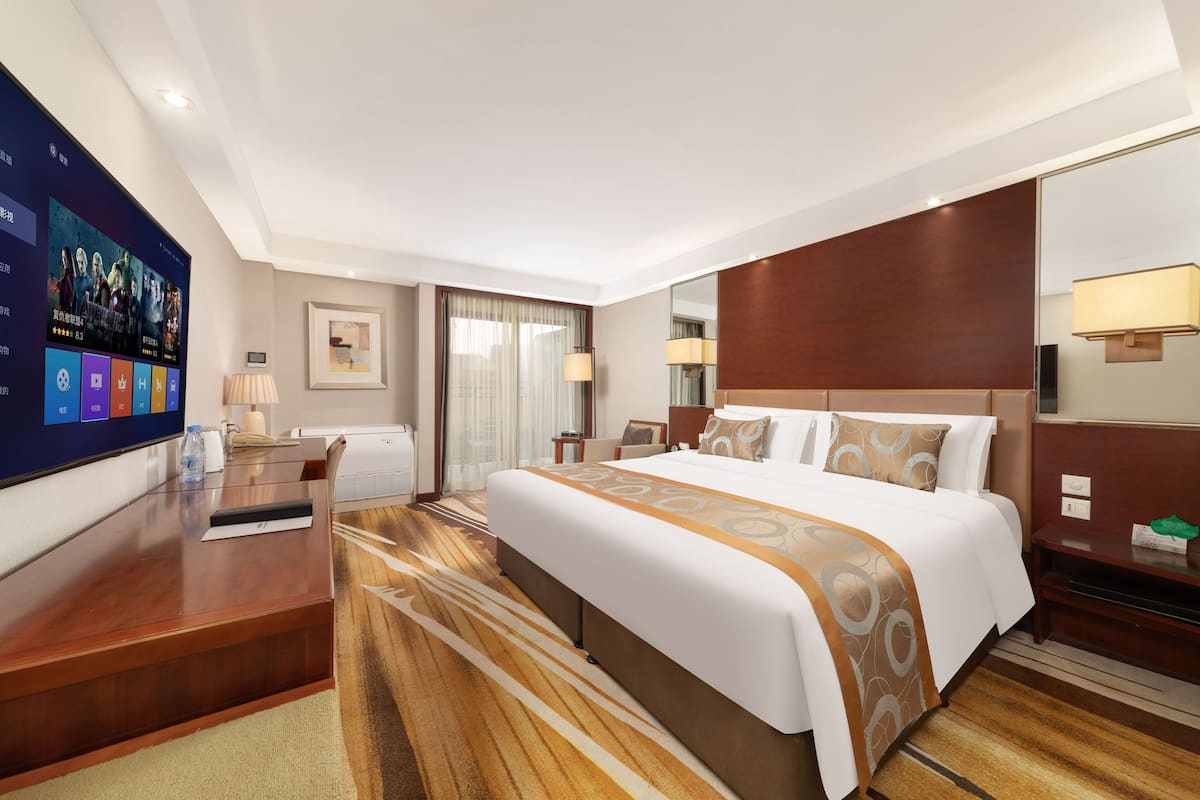 Ein Hotelzimmer mit einem großen Bett, einem Schreibtisch, einem Flachbildfernseher, einem Nachttisch und einem Spiegel.