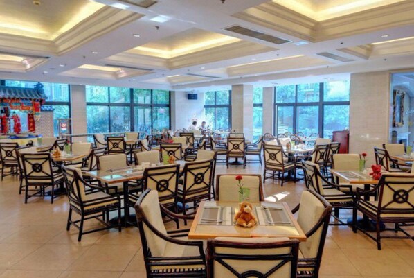 Un restaurant spacieux, doté de nombreuses tables et chaises, de grandes fenêtres et d’un élément décoratif traditionnel en arrière-plan.