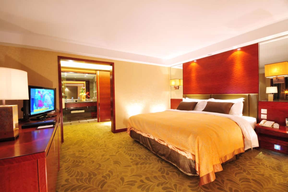 Ein Hotelzimmer mit einem großen Bett, einem Fernseher, einem Schreibtisch mit einer Lampe und einem Spiegel.