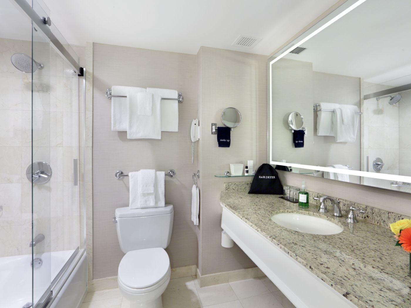 A modern bathroom with a glass shower enclosure, a toilet, a sink with a granite countertop, and a large mirror.
