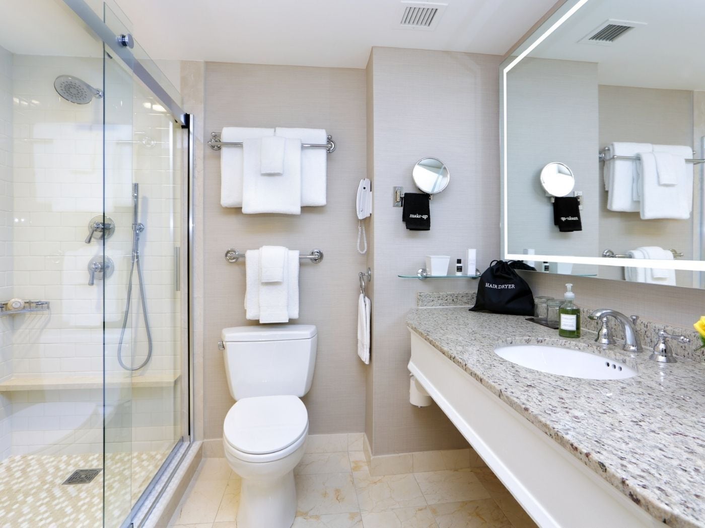 A modern bathroom with a glass shower enclosure, a toilet, a sink with a granite countertop, and a large mirror.