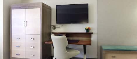 A hotel room with a bed, a desk with a chair, a television, a wardrobe, and a bedside table.