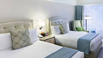 A hotel room with two beds, a chair, a nightstand with a lamp, and a window with curtains.