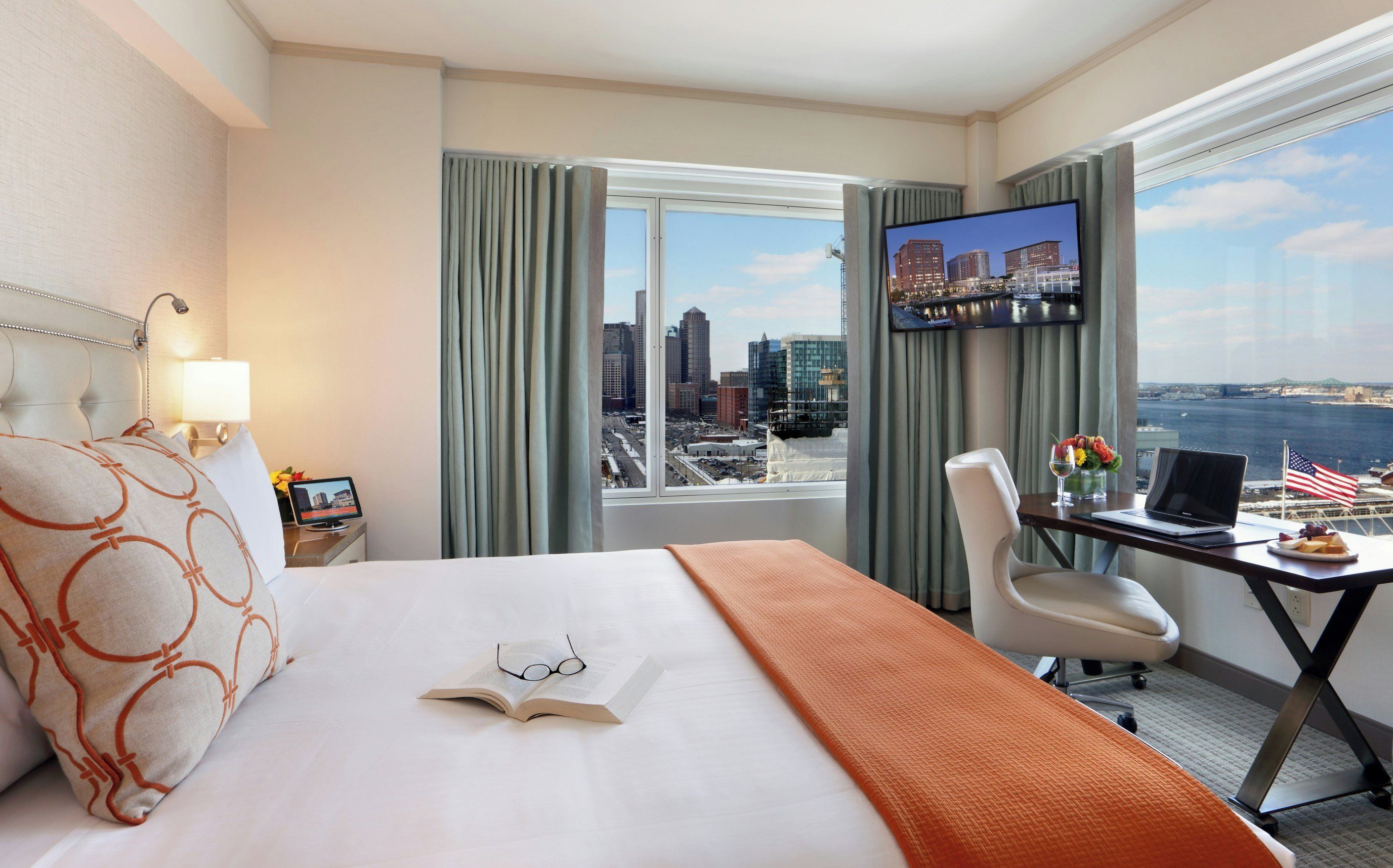 Habitación de hotel con cama, escritorio, computadora portátil, televisión y vista a la ciudad.
