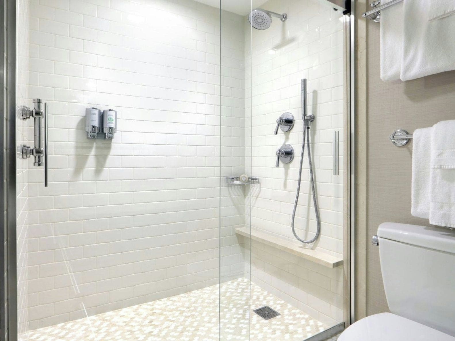 A modern bathroom with white tiled walls, a glass shower enclosure, a toilet, and a towel rack.
