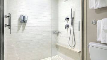 A modern bathroom with white tiled walls, a glass shower enclosure, a toilet, and a towel rack.