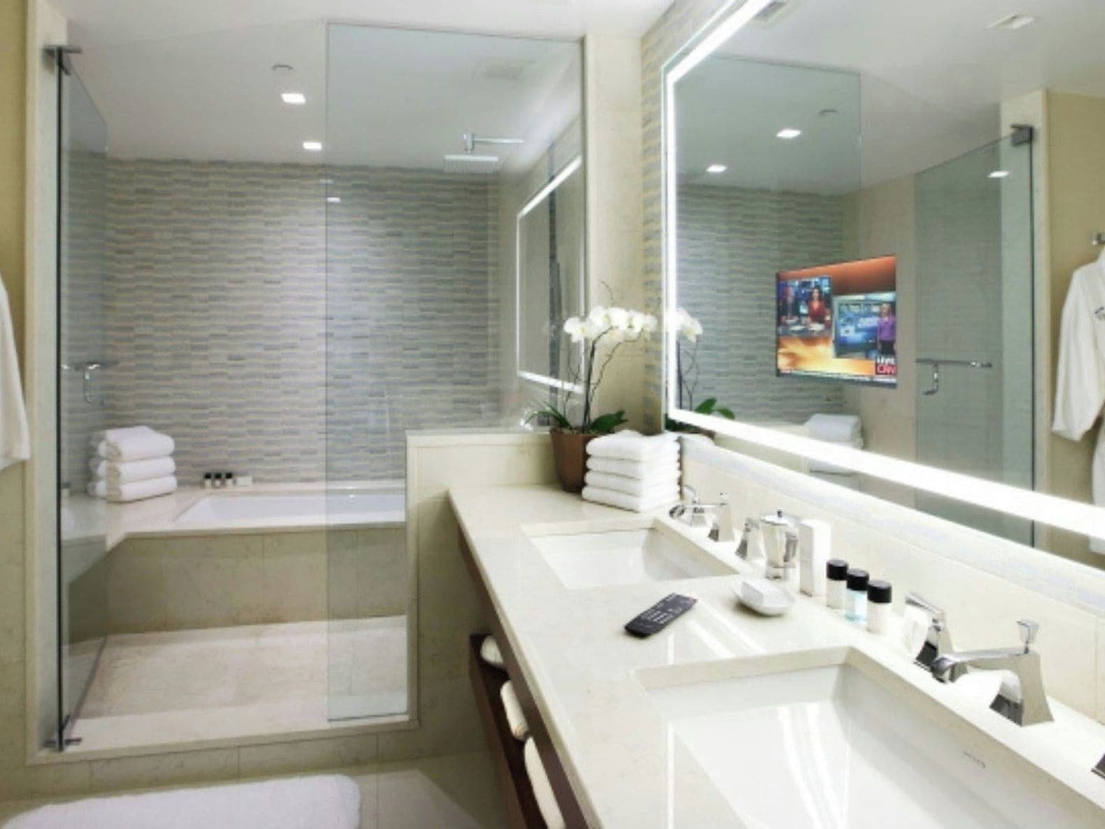 A modern bathroom with a glass shower enclosure, a large mirror, and a vanity with a sink and countertop.