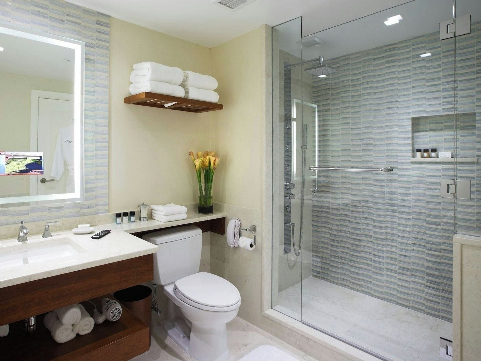 Une salle de bain moderne avec une douche à parois de verre, des toilettes blanches, un meuble-lavabo avec un miroir et une étagère avec des serviettes.