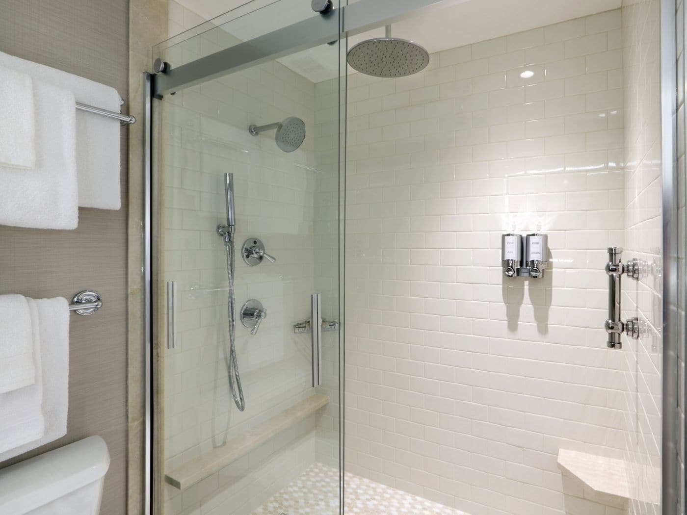 A modern shower with a glass enclosure, a handheld showerhead, and a wall-mounted control panel.