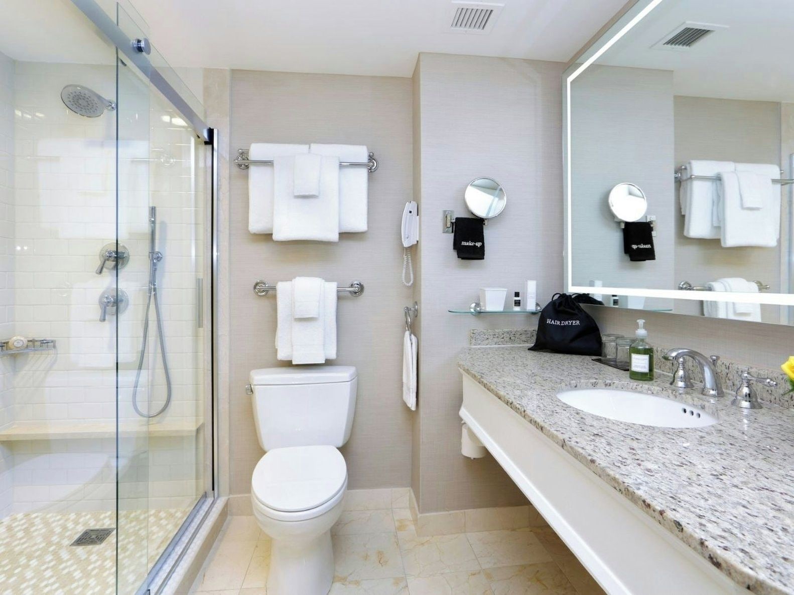 A modern bathroom with a glass-enclosed shower, a toilet, a sink with a mirror, and a hair dryer bag on the countertop.