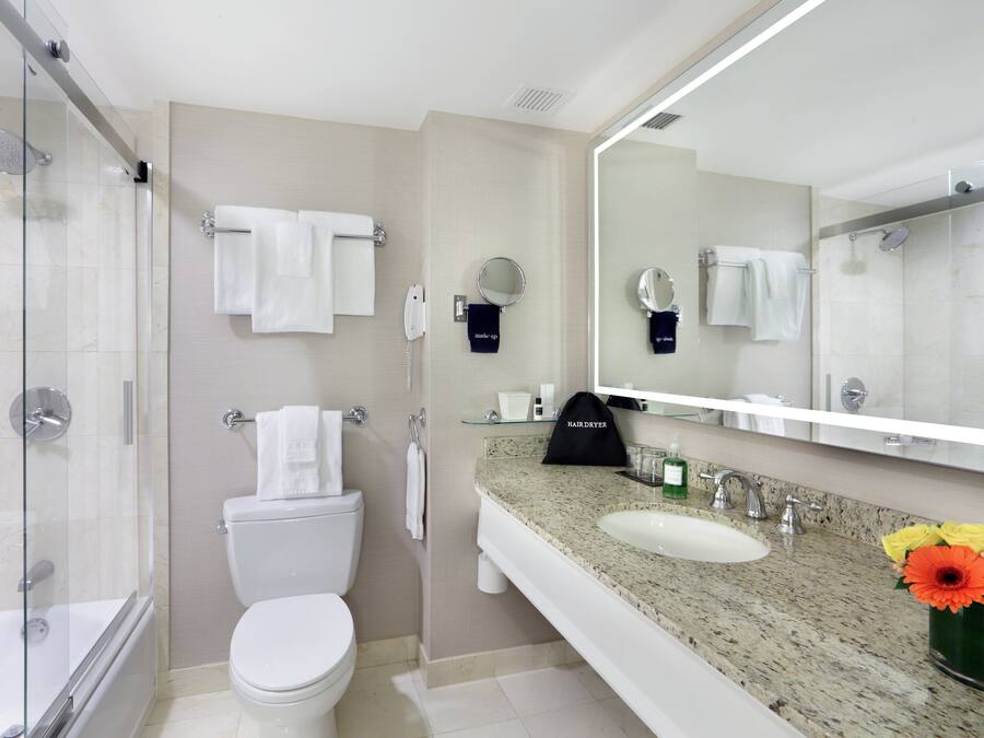 Un baño moderno con ducha de vidrio, inodoro, lavabo con encimera de granito y un espejo grande.