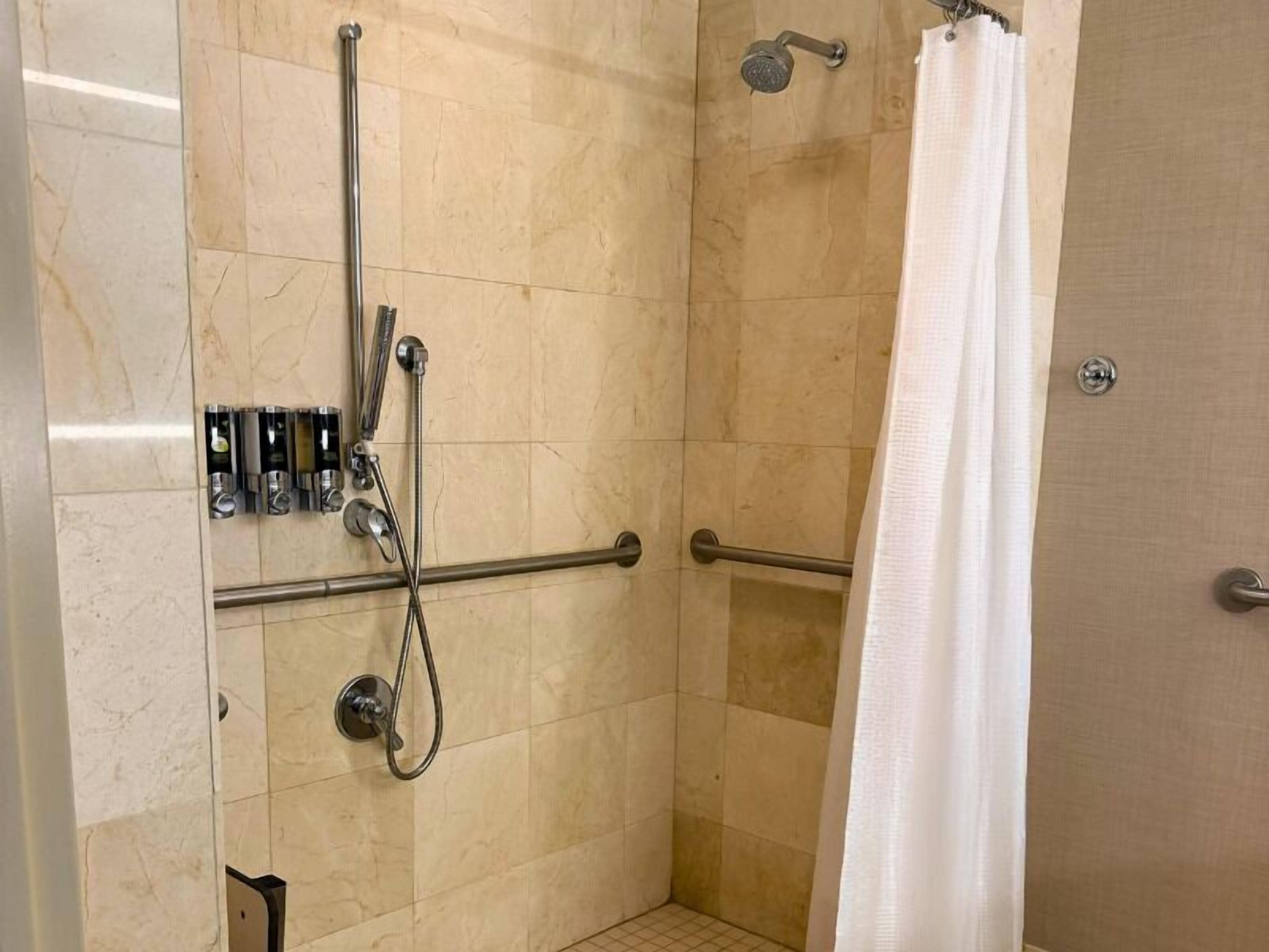 A shower area with a grab bar, a handheld showerhead, and a shower caddy.