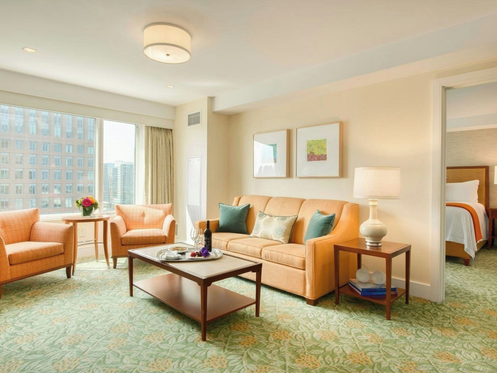 A hotel room with a sofa, armchair, coffee table, and a bed with a nightstand.
