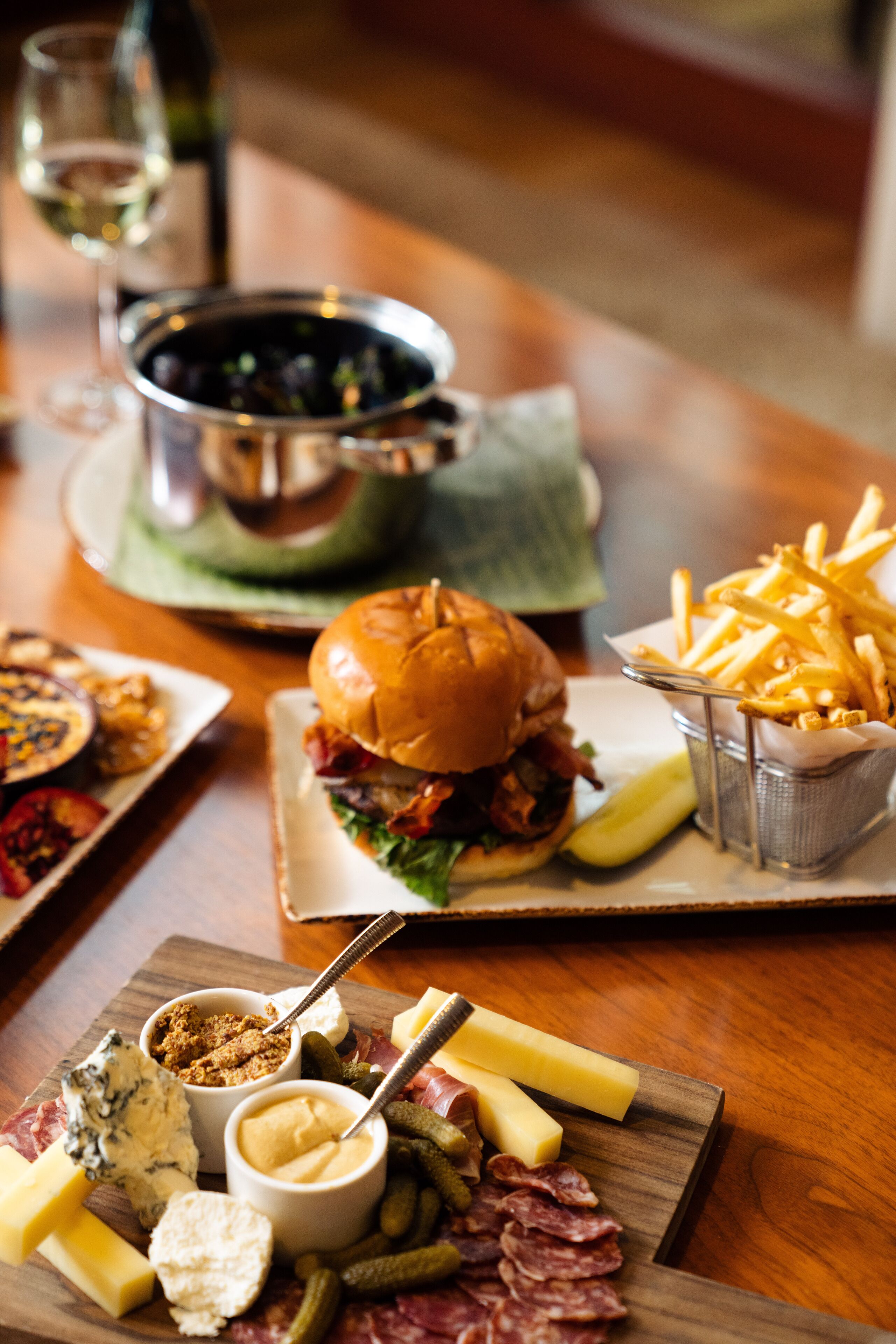 A wooden table with a variety of food items including a burger, fries, cheese, and pickles.