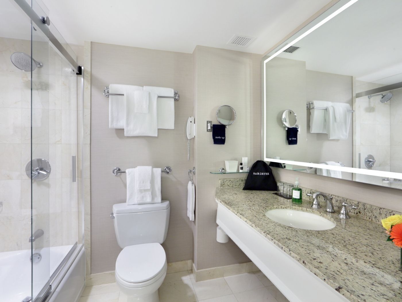 A modern bathroom with a glass-enclosed shower, a toilet, a sink with a granite countertop, and a large mirror.