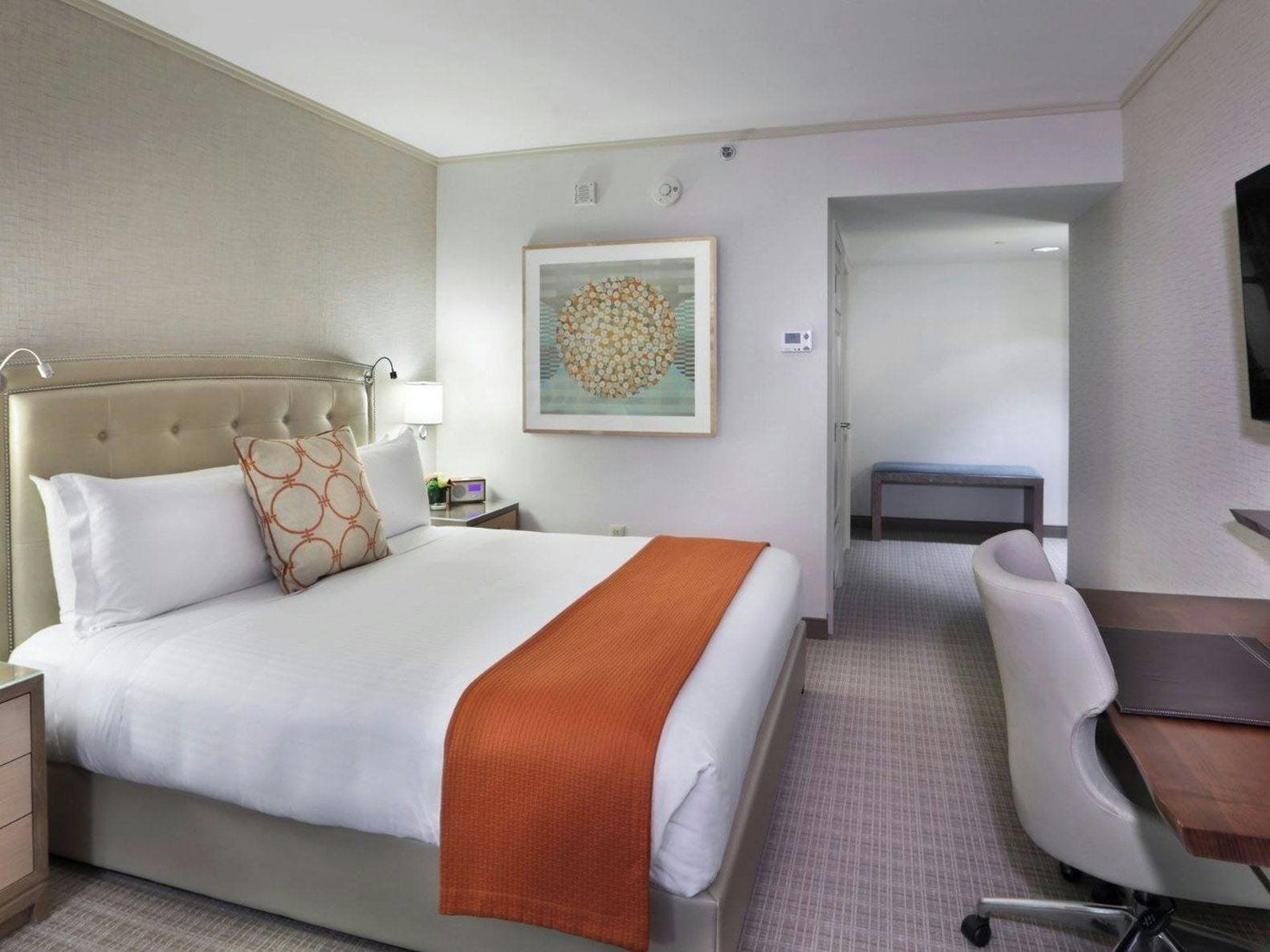 Una habitación de hotel con una cama, mesita de noche, lámpara y un escritorio con una silla.