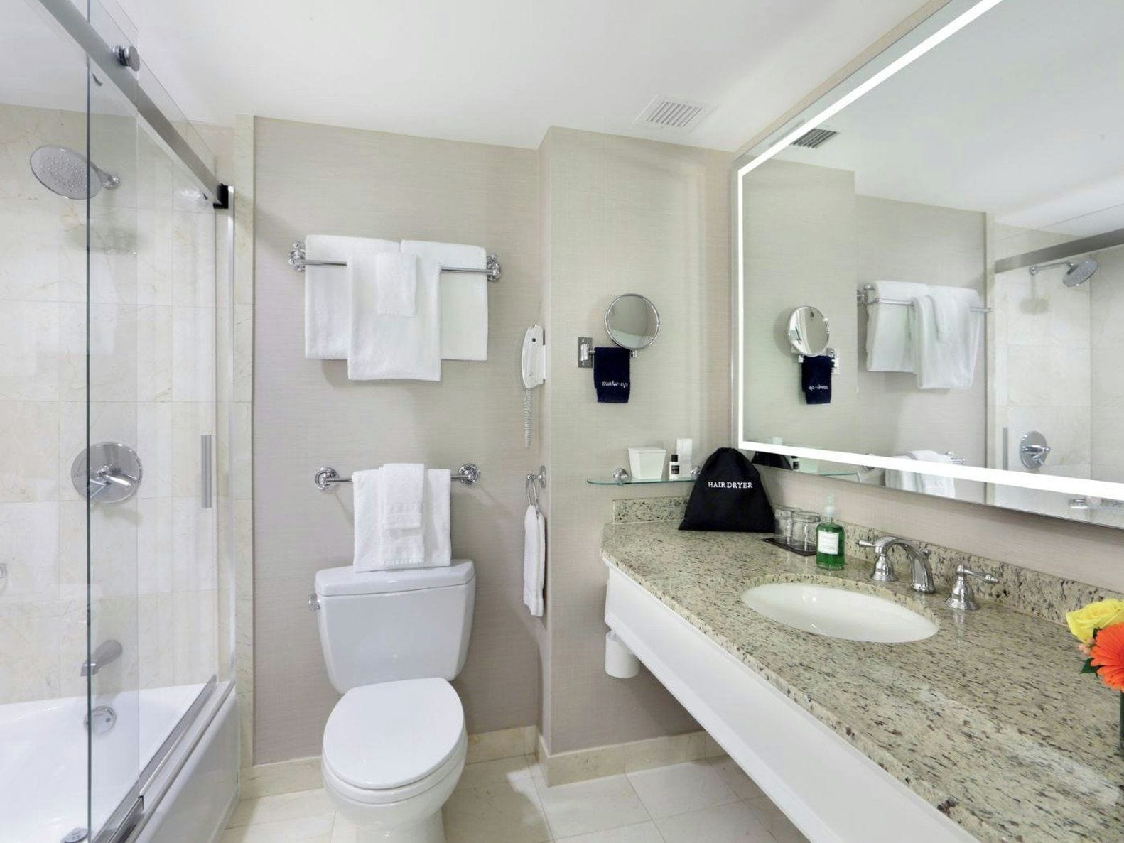 Un baño moderno con ducha envuelta en vidrio, un inodoro, un lavamanos con encimera de granito y un espejo grande.
