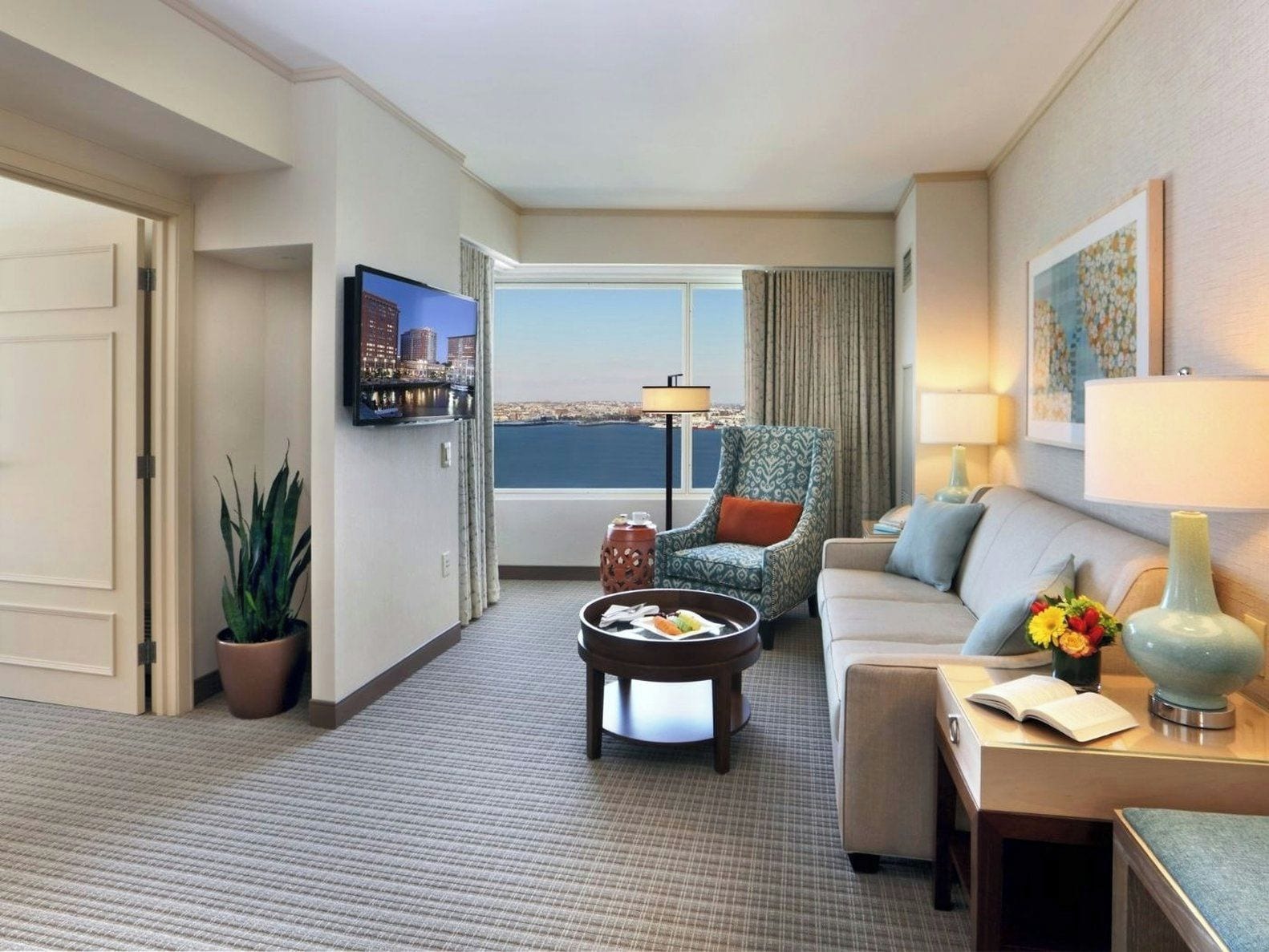 Ein Hotelzimmer mit Sofa, Sessel, Couchtisch, Fernseher und Blick auf die Stadt.