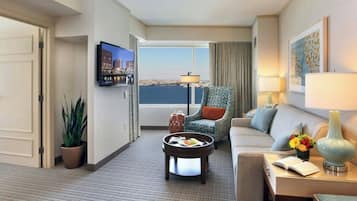 Ein Hotelzimmer mit Sofa, Sessel, Couchtisch, Fernseher und Blick auf die Stadt.